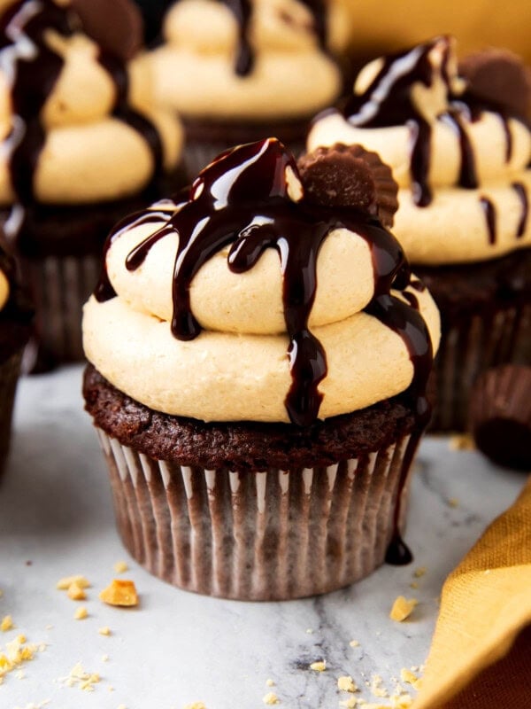 Chocolate cupcakes with peanut butter cups are topped with peanut butter frosting and chocolate drizzle