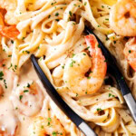 Tongs grabbing easy shrimp Alfredo with frozen shrimp, linguine, and lots of homemade Alfredo sauce