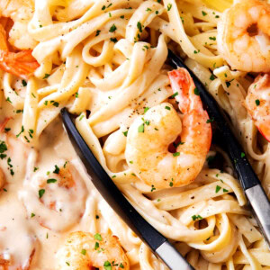 Tongs grabbing easy shrimp Alfredo with frozen shrimp, linguine, and lots of homemade Alfredo sauce