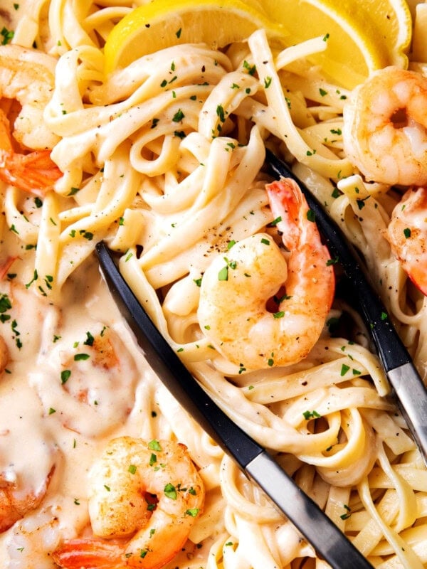 Tongs grabbing easy shrimp Alfredo with frozen shrimp, linguine, and lots of homemade Alfredo sauce