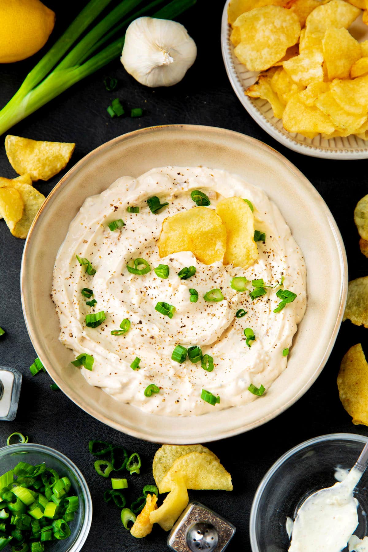 Recipe for clam dip is served in a bowl with potato chips topped with chives.
