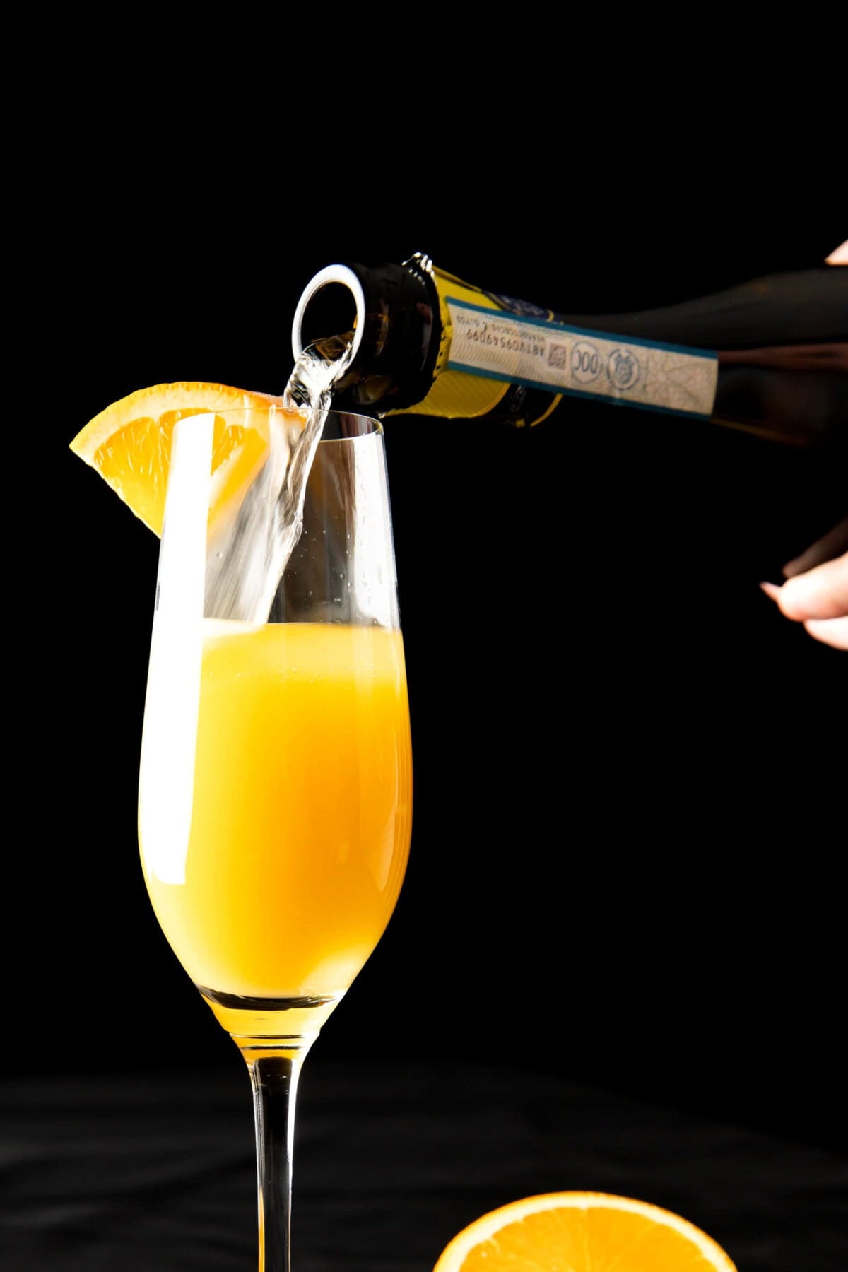 Someone pouring Prosecco into a champagne flute half-filled with orange juice.