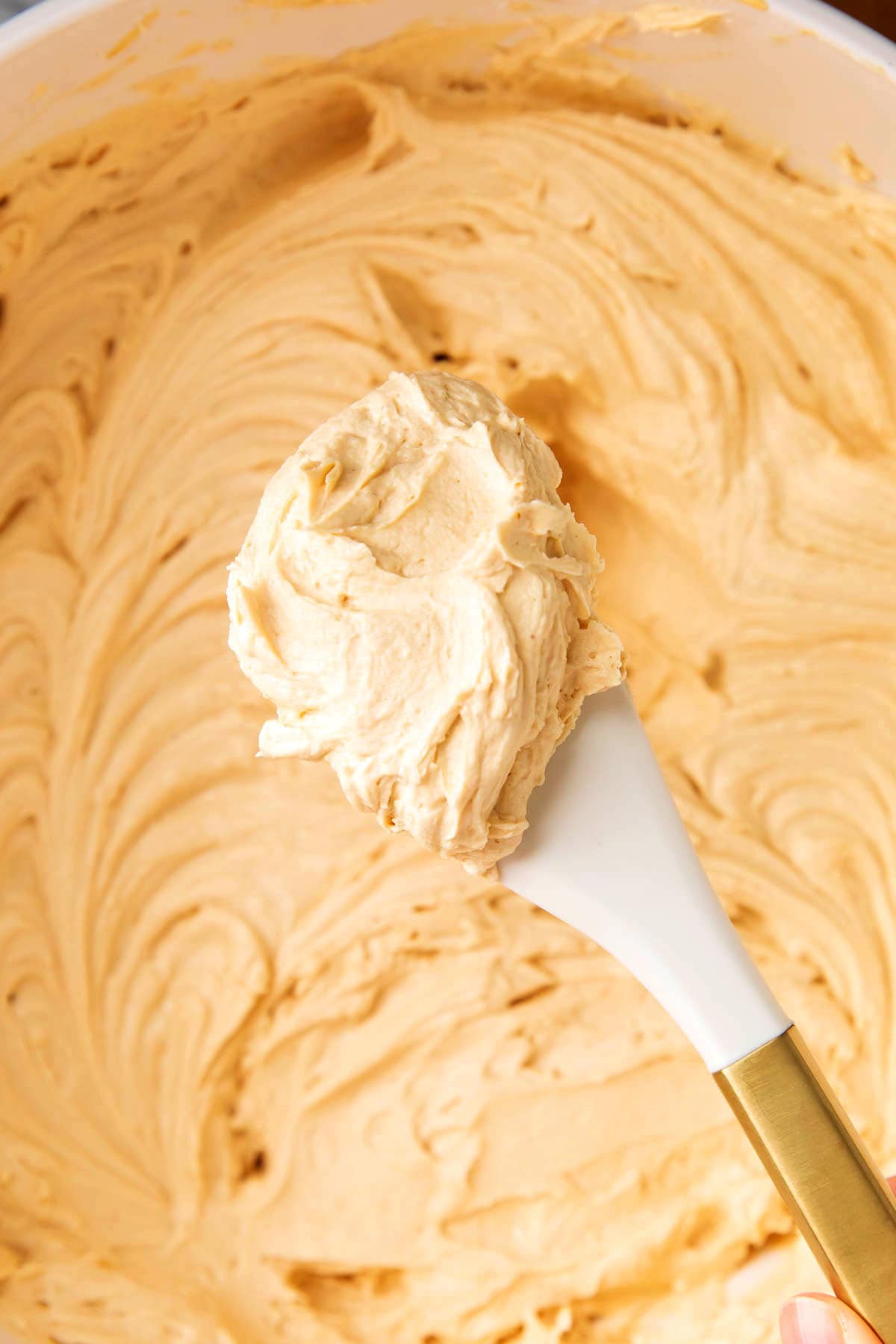 Frosting spatula scooping up fluffy peanut butter frosting to show smooth texture.