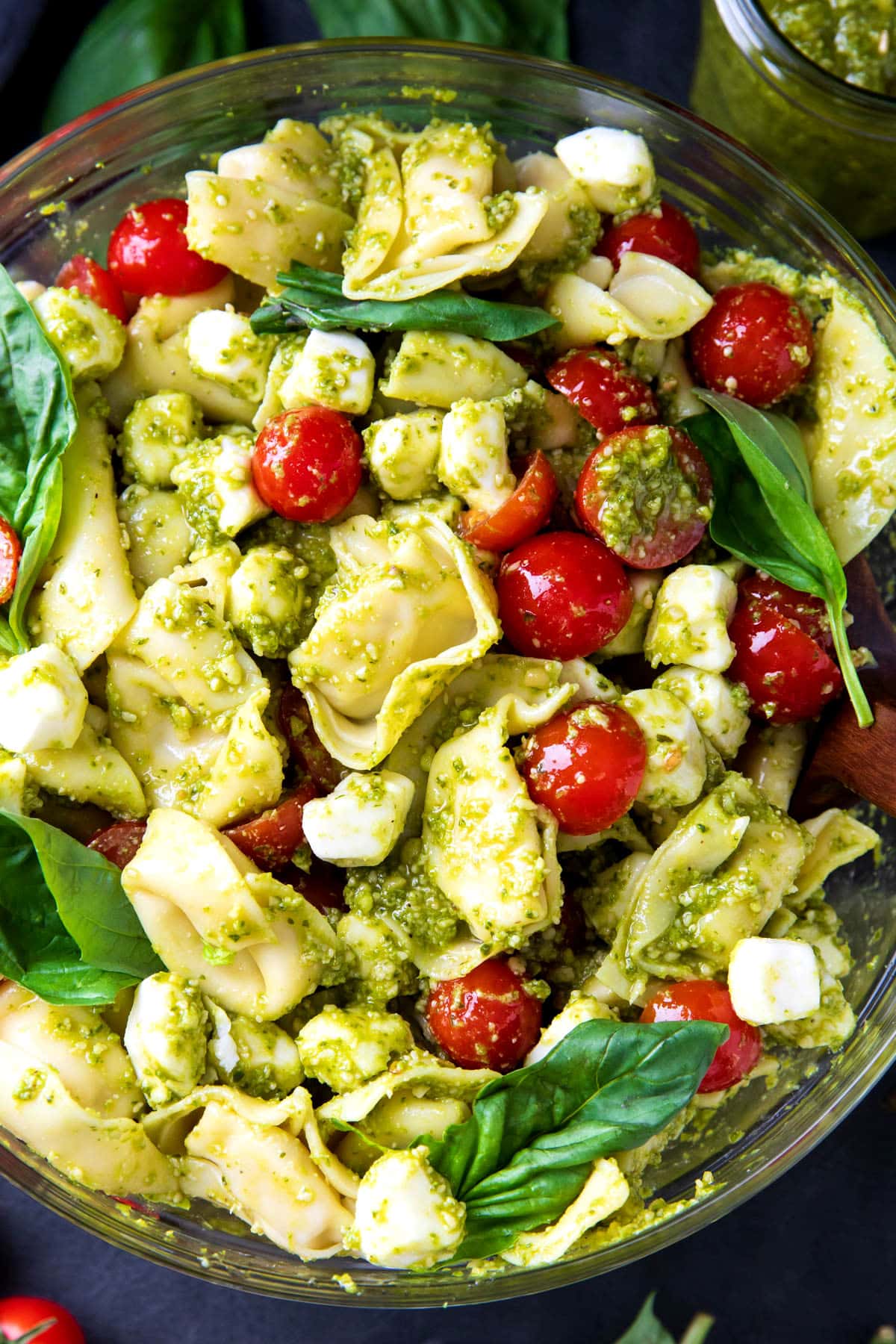 Serving bowl with pesto tortellini pasta salad with cheese tortellini, cherry tomatoes, and mozzarella pearls.