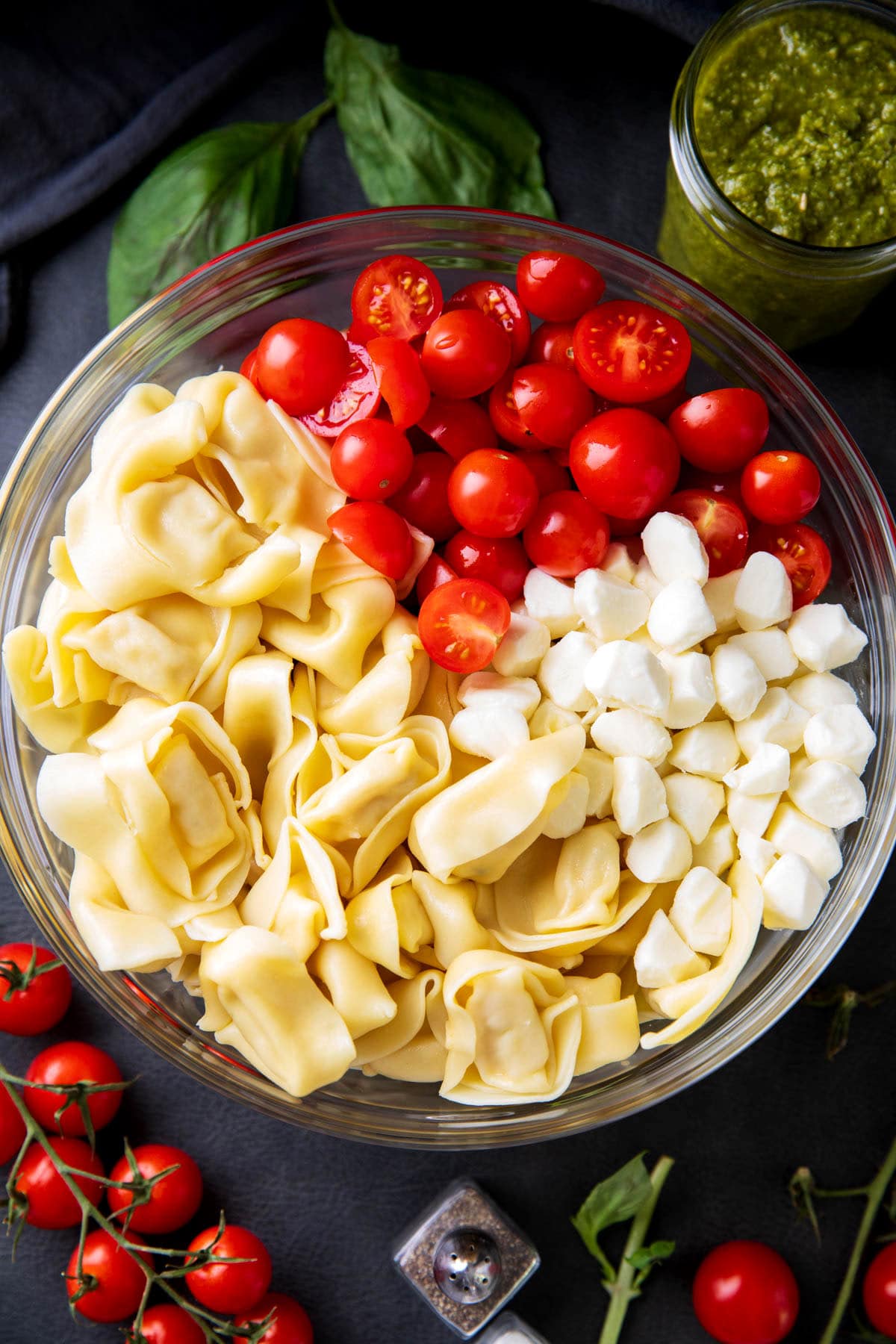 A photo showing how to make tortellini pesto pasta salad - tortellini, mozzarella, and cherry tomatoes arranged in a bowl.