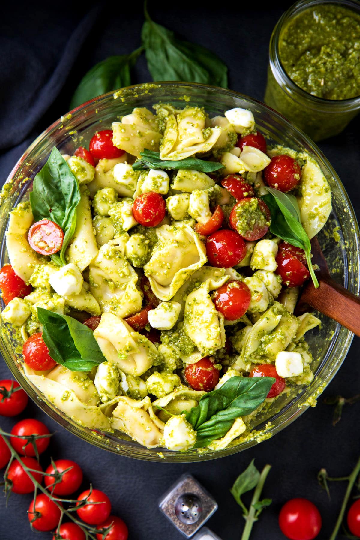 Easy pesto pasta salad with tortellini, basil pesto sauce, mozzarella cheese, cherry tomatoes in a mixing bowl.