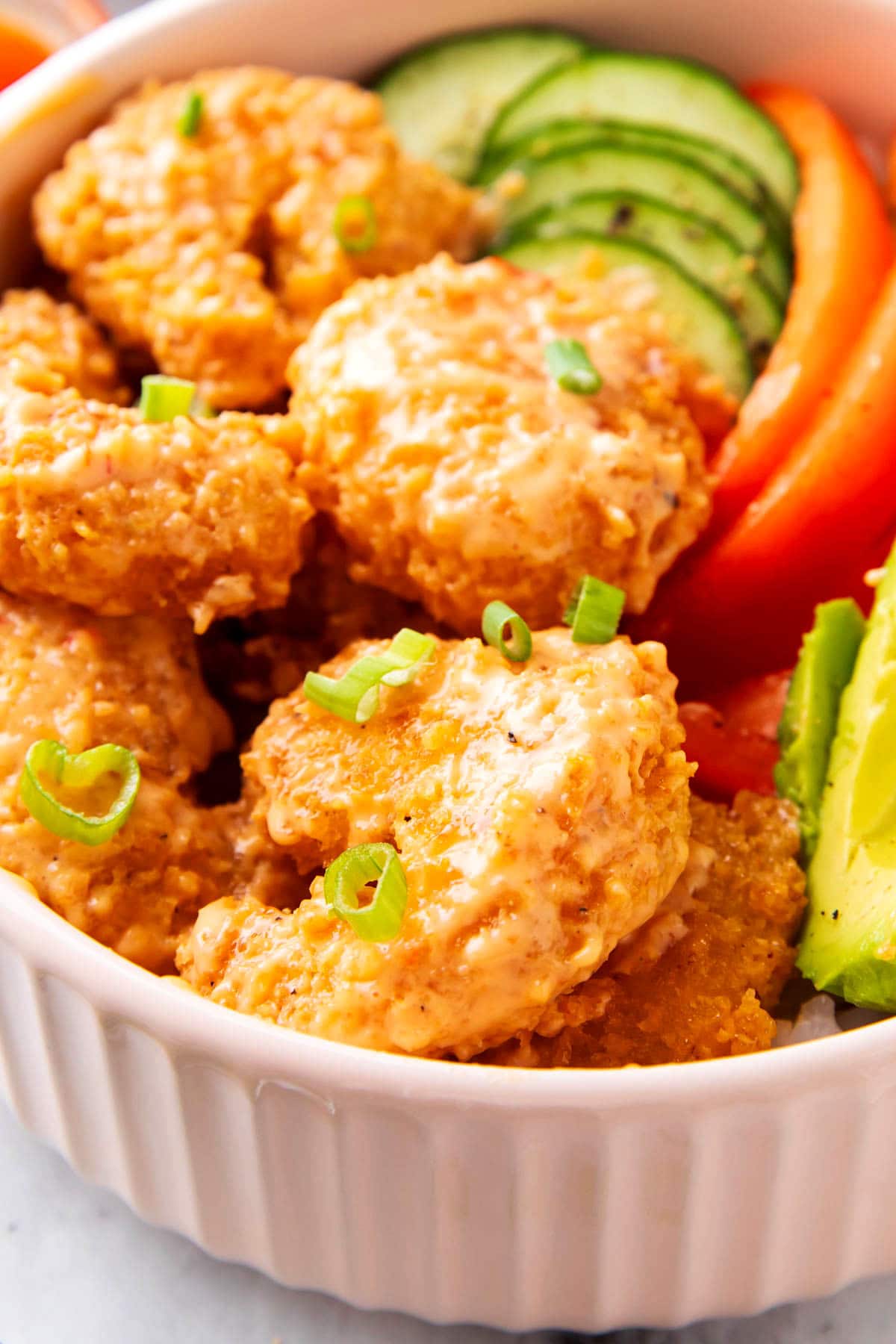 This bang bang shrimp bowl includes sliced fresh cucumbers, avocado and bell peppers served with bang bang bang shrimp on rice.