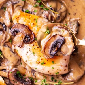 Close up of someone spooning chicken breast with creamy mushroom sauce in this creamy chicken and mushroom skillet