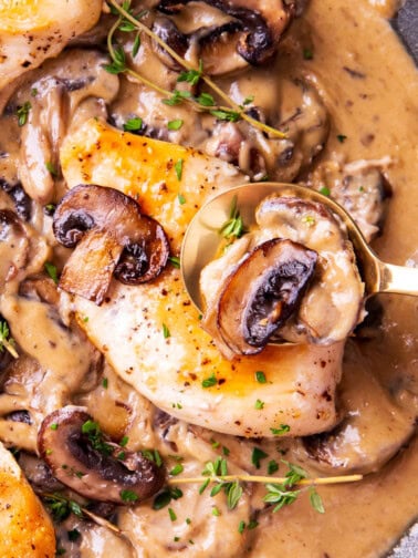 Close up of someone spooning chicken breast with creamy mushroom sauce in this creamy chicken and mushroom skillet