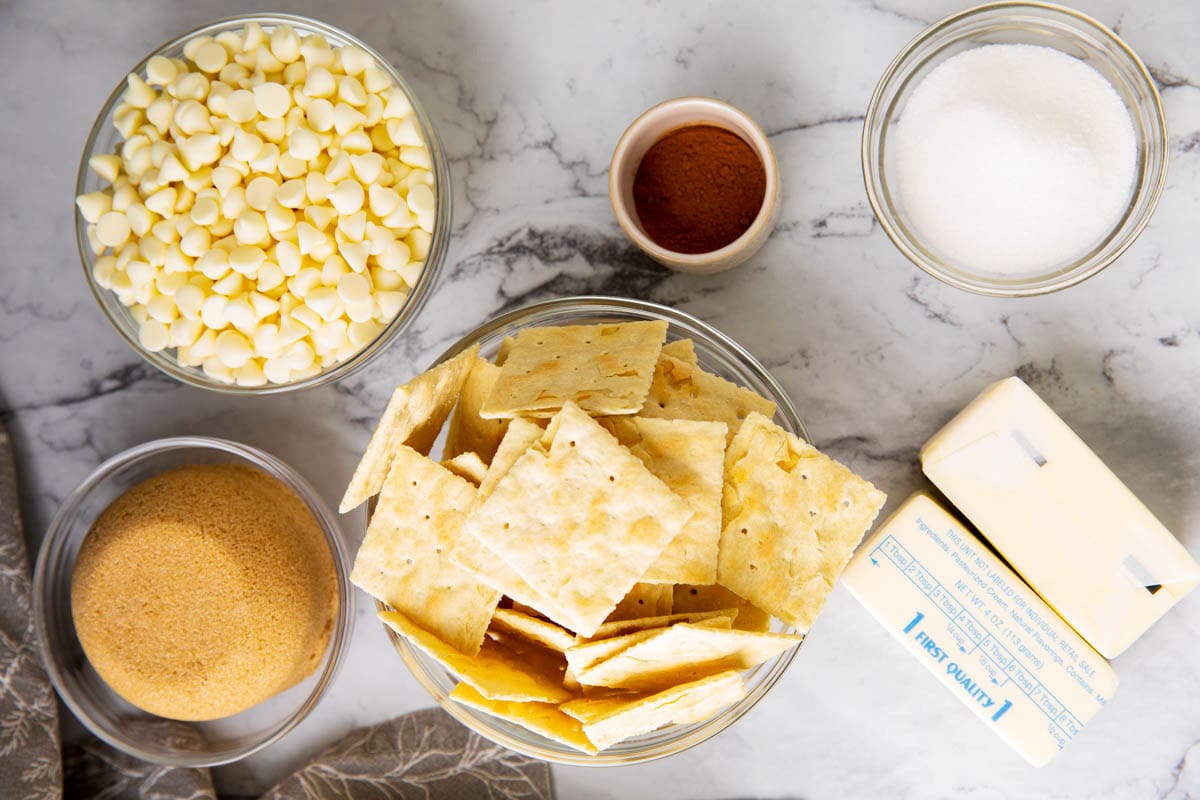 Churro crack recipe ingredients measured in bowls including saltine crackers, white chocolate, brown sugar, butter, cane sugar, and ground cinnamon.