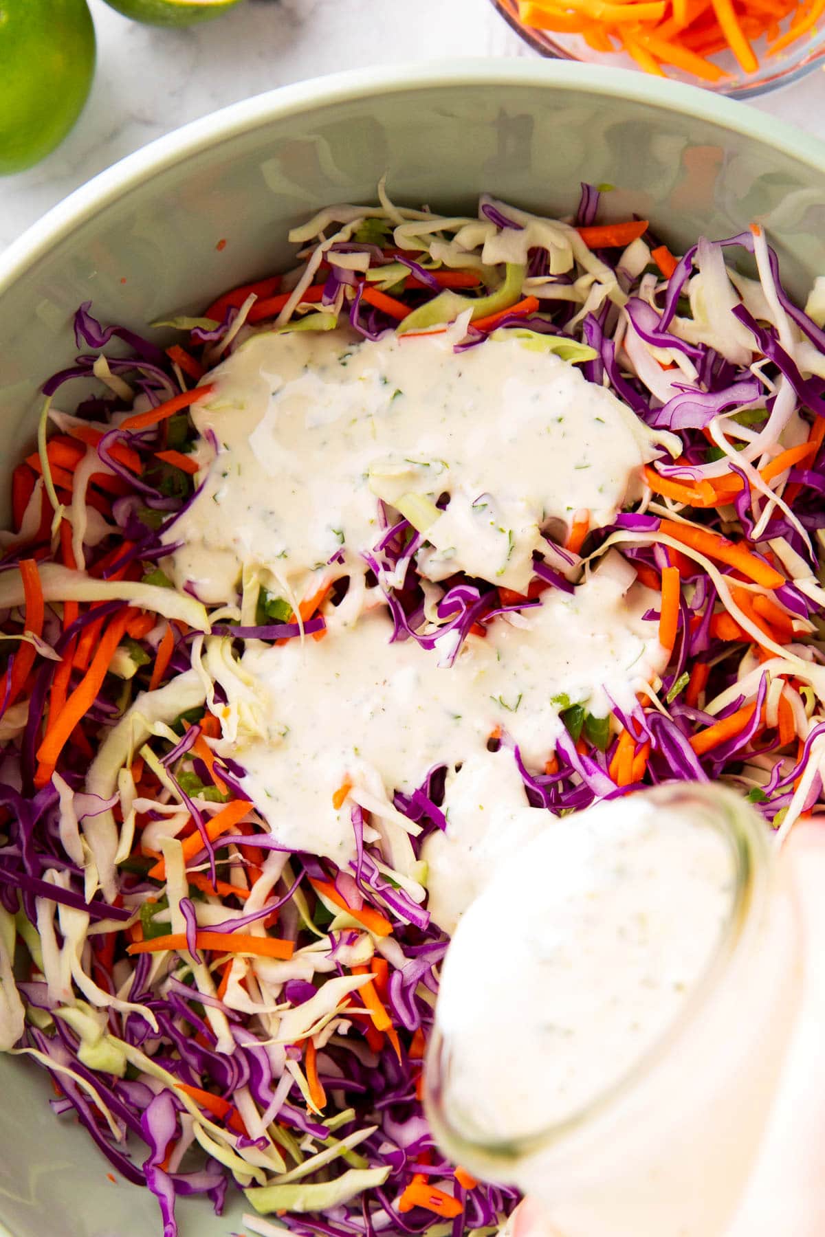 Close up of someone pouring dressing over cilantro lime cabbage cole slaw