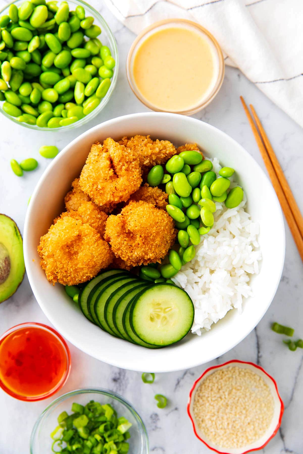 Shrimp rice bowls on a table with sesame seeds, chopsticks, Thai sweet chili, and yum yum sauce.