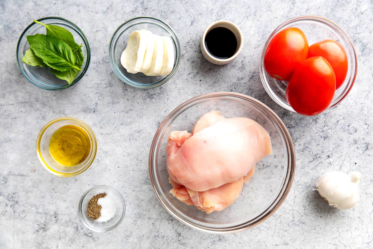 Easy bruschetta chicken ingredients in bowls, including chicken breasts, tomatoes, balsamic vinegar, garlic, mozzarella, basil, olive oil, salt and pepper.