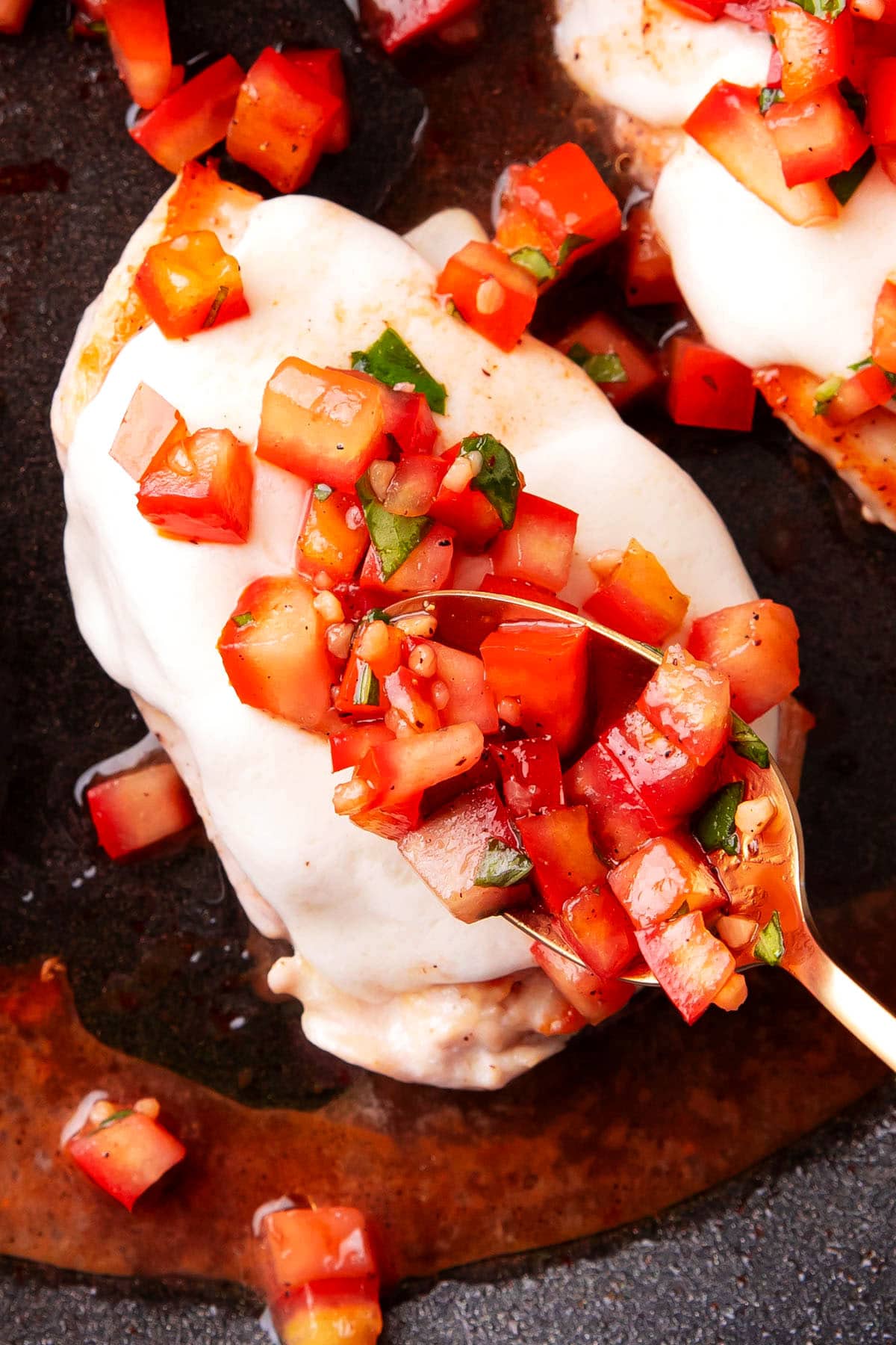 The last step in this easy bruschetta chicken recipe is spooning bruschetta on top of the melted mozzarella on chicken.