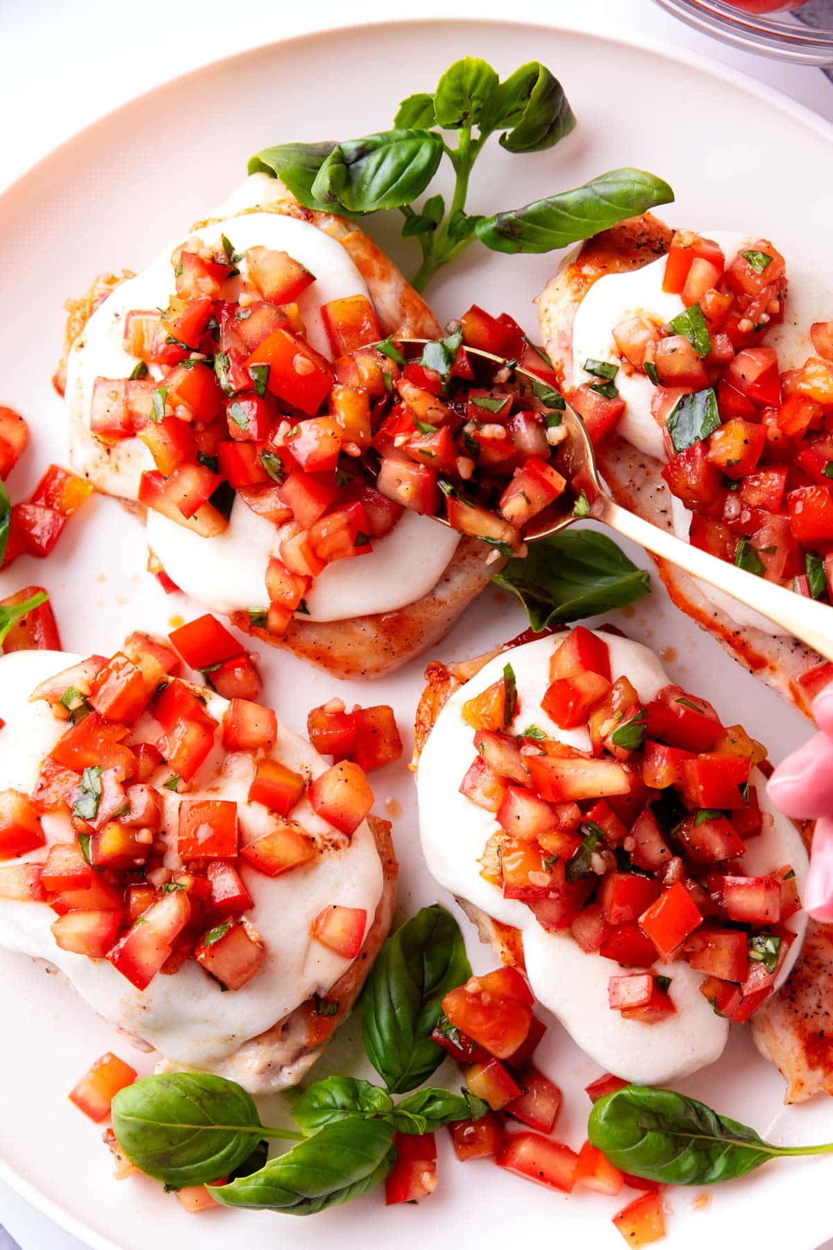 Someone spooning basil packed bruschetta on top of this easy bruschetta chicken.