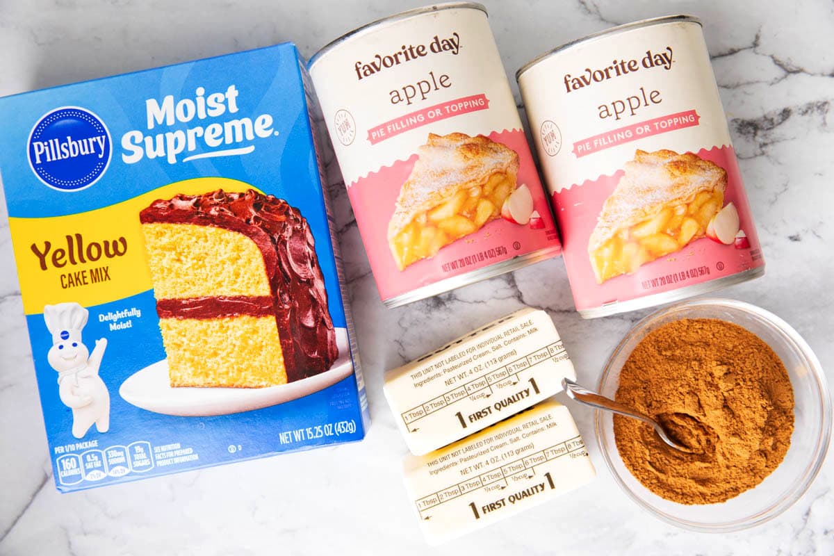 The ingredients for Apple Dump Cake including cake mix, butter, apple pie filling, and apple pie spice mix.