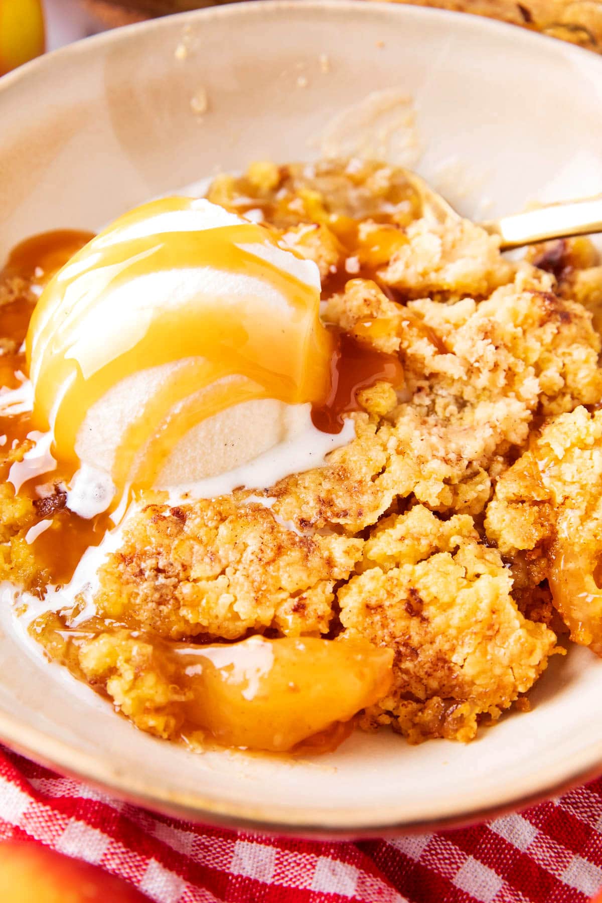 Close up showing a scoop of ice cream served with this fall baked recipe in a bowl filled with buttery crumb topping and fruit peeking out of the warm filling