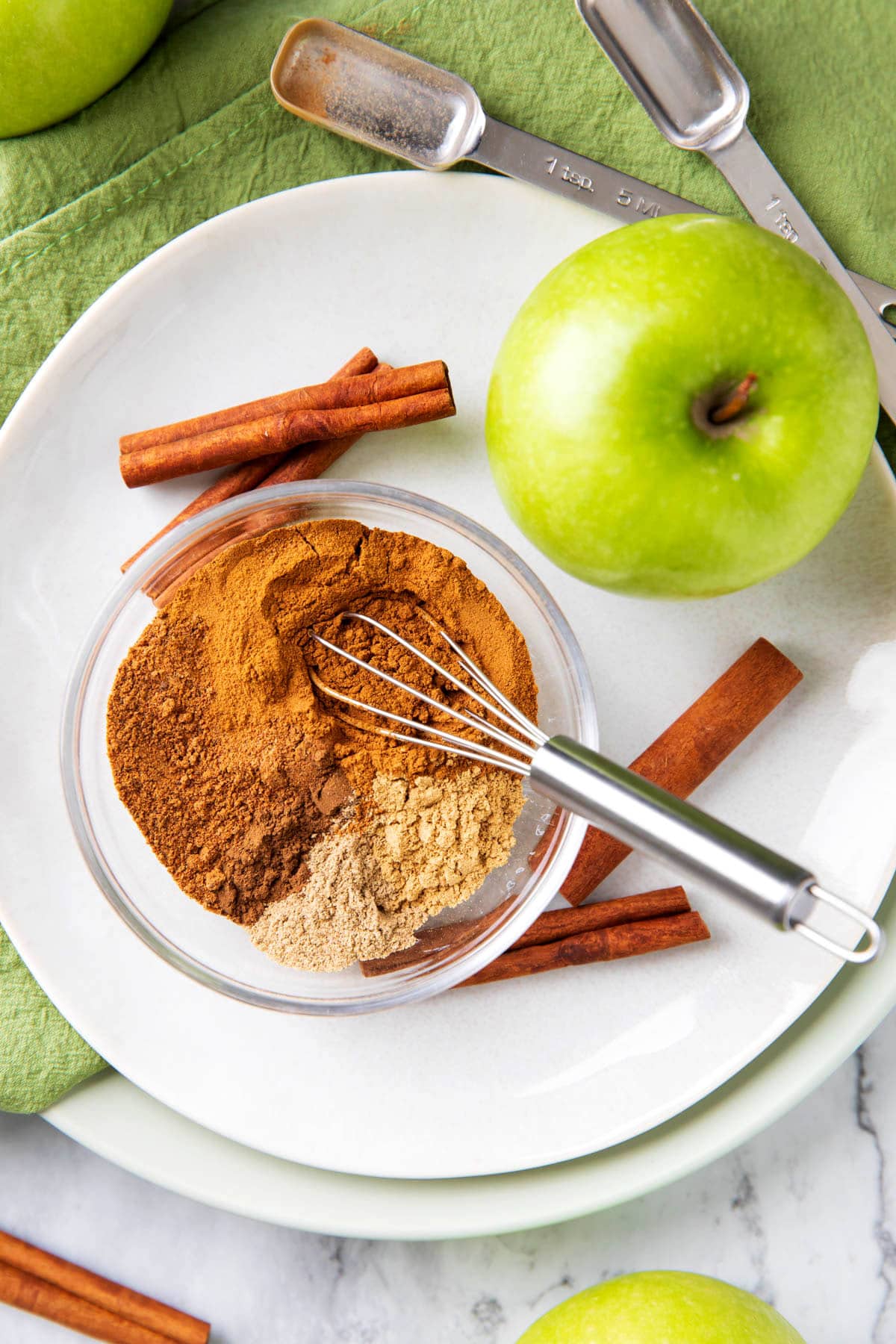 Apple Pie Spice on a table with cinnamon and apples.