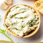 Garlic Butter served in a bowl on a platter with a spreader, toasted bread, garlic, and chives