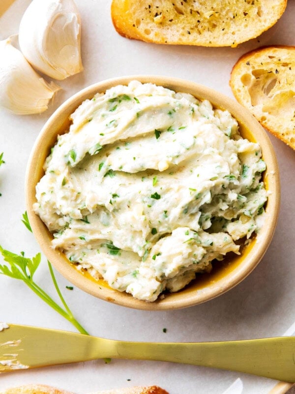 Garlic Butter served in a bowl on a platter with a spreader, toasted bread, garlic, and chives