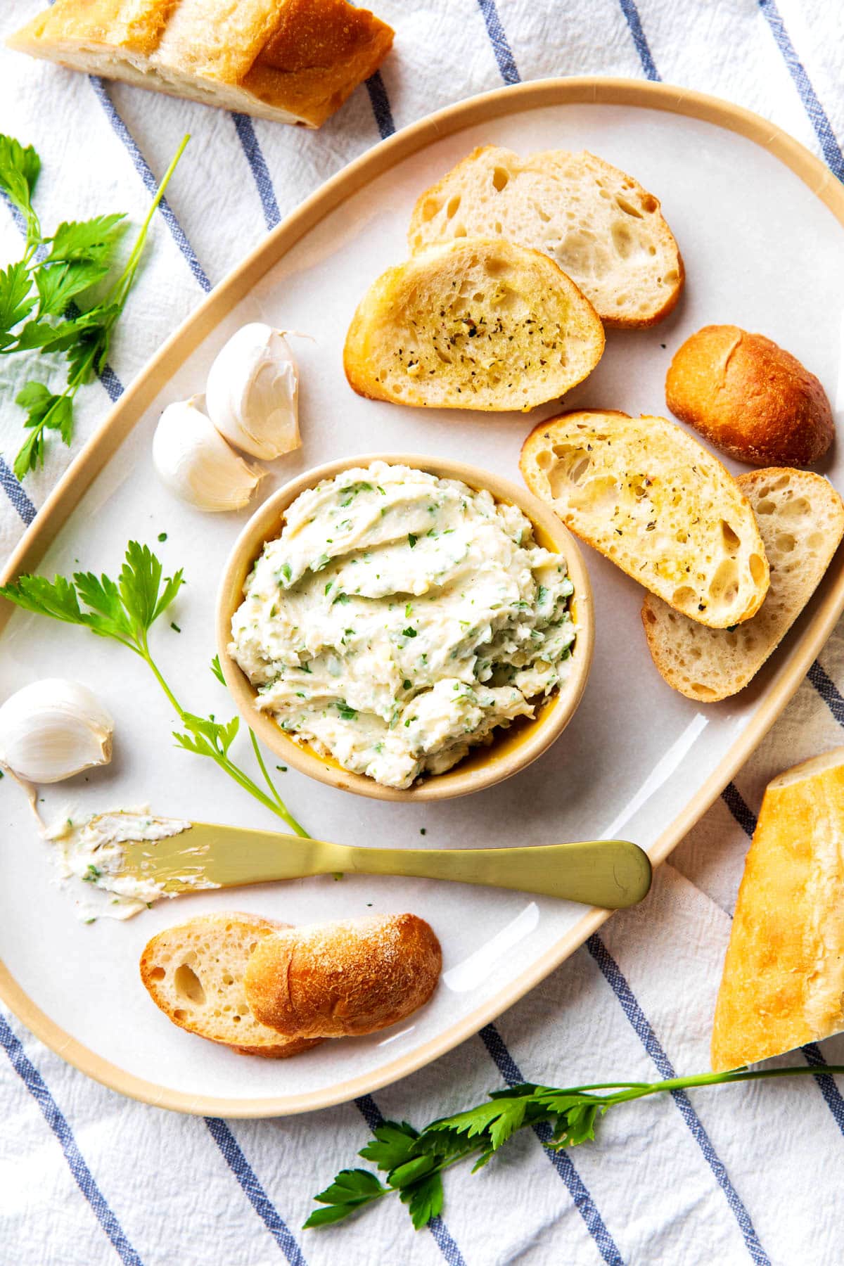 This chive spread is served on a platter with crostini bread and cloves of garlic.