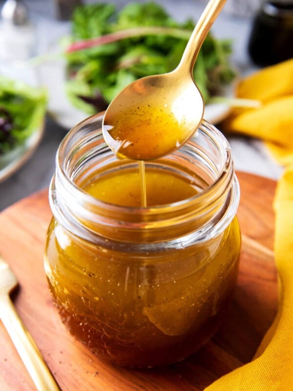 Close up of someone holding a spoonful of Maple Vinaigrette dribbling it down into a salad dressing jar