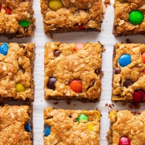 Fresh-baked Monster Cookie Bars sit on parchment paper with oats and M&M's near