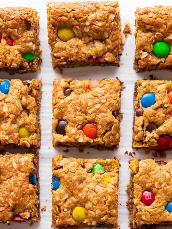 Fresh-baked Monster Cookie Bars sit on parchment paper with oats and M&M's near