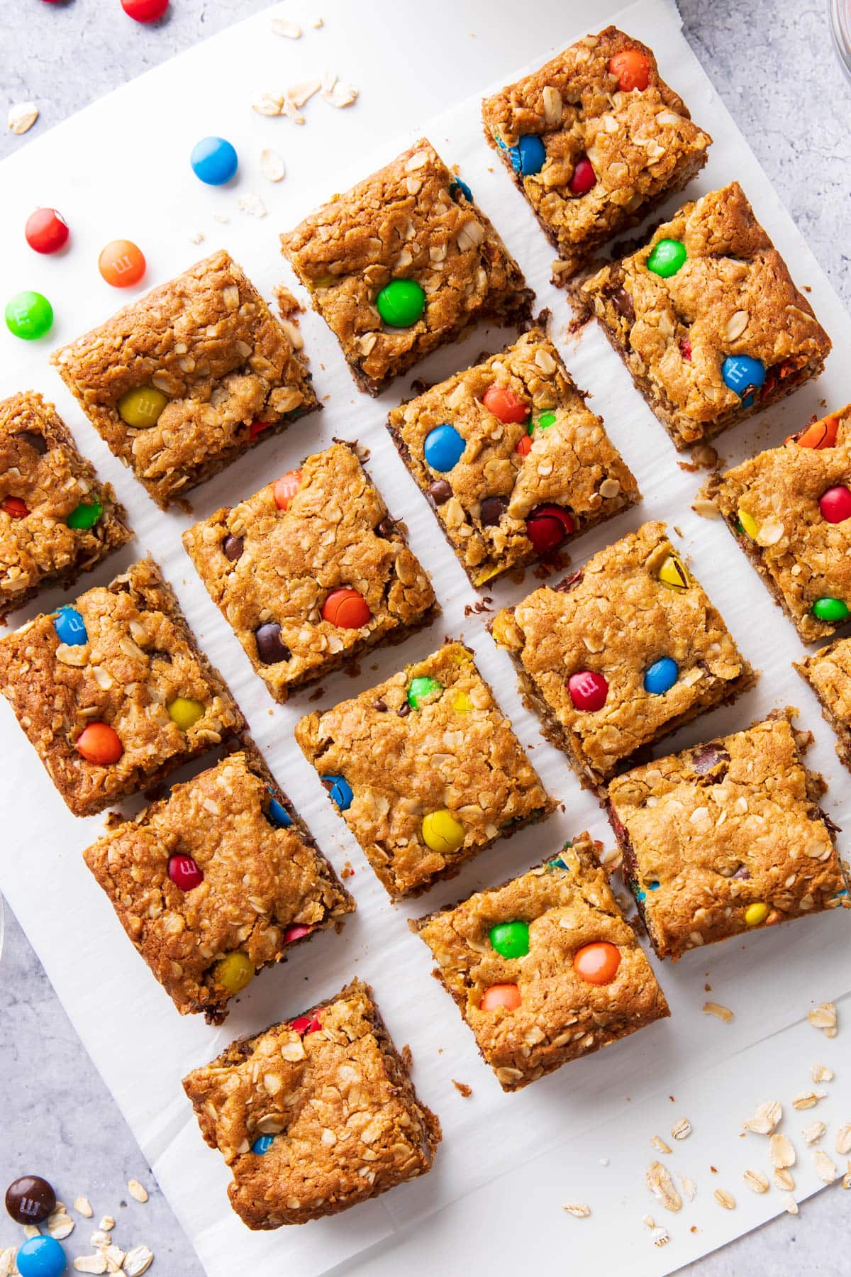 Thick and chewy bars sliced on parchment paper with oats and candies.