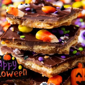 A stack of Halloween Crack shows the delicious layers of toffee-coated saltine crackers with chocolate topping and Halloween decorations on top