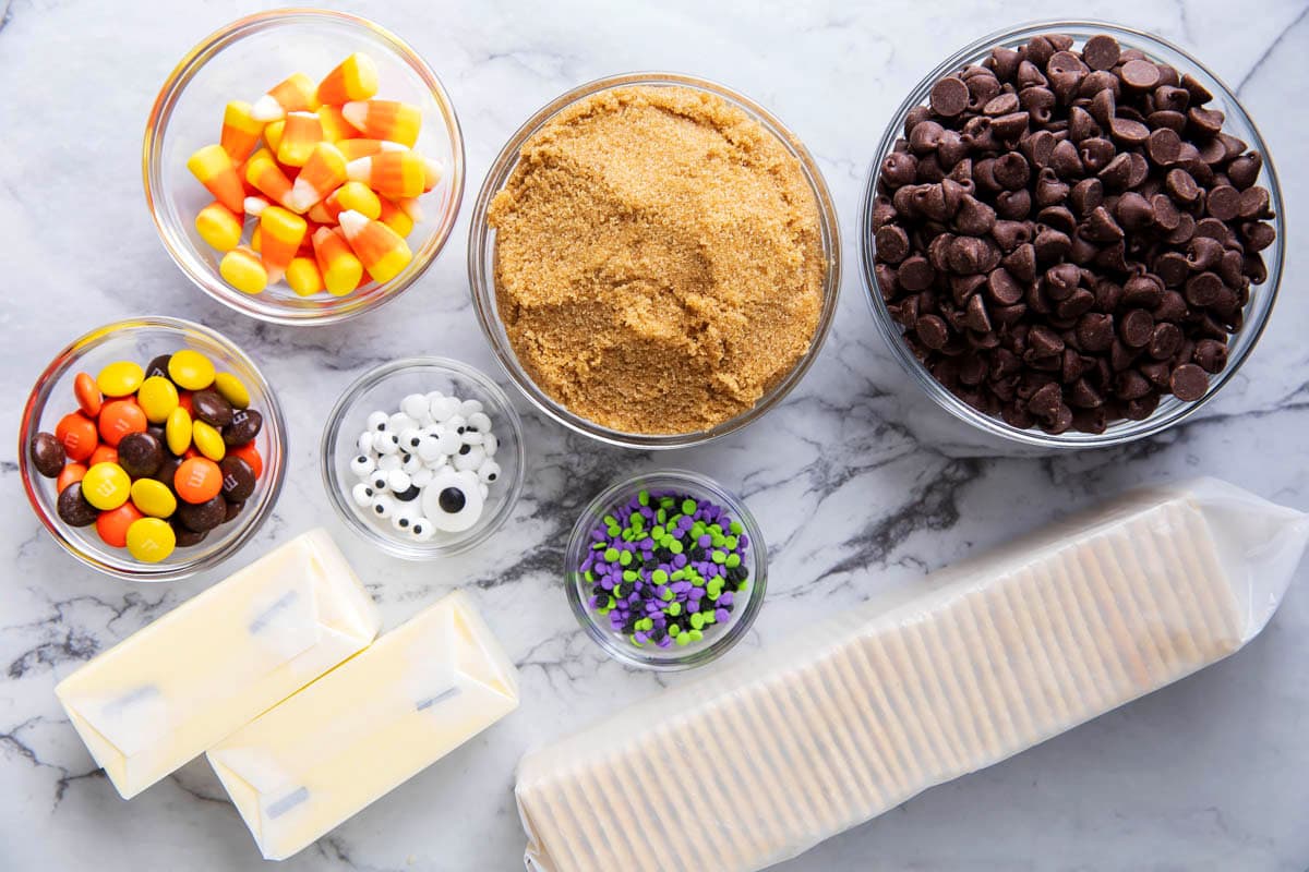 Halloween Crack ingredients including saltine crackers, butter, brown sugar, chocolate chips, Halloween sprinkles, candy corn, and festive M&M's candies.