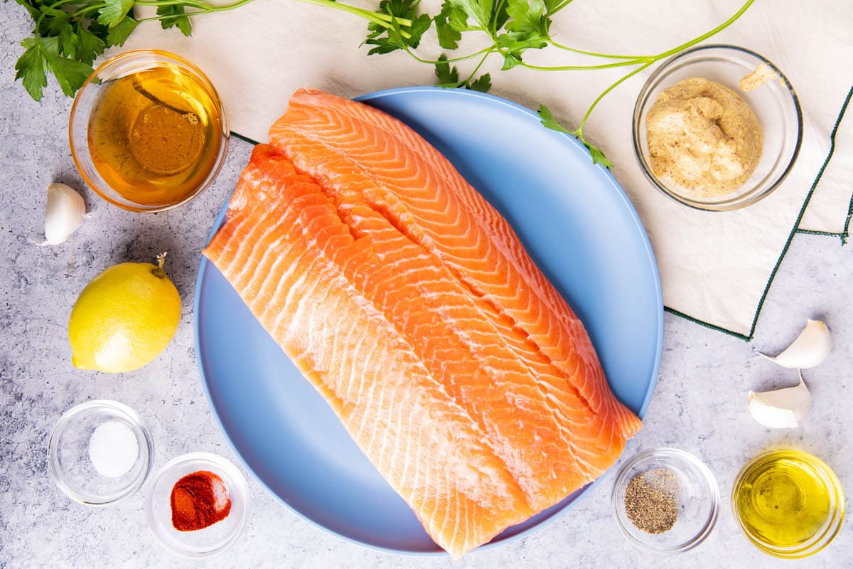 Honey Mustard Salmon ingredients including salmon, whole grain mustard, honey, olive oil, garlic, lemon juice, smoked paprika, salt, pepper, lemons, and parsley.
