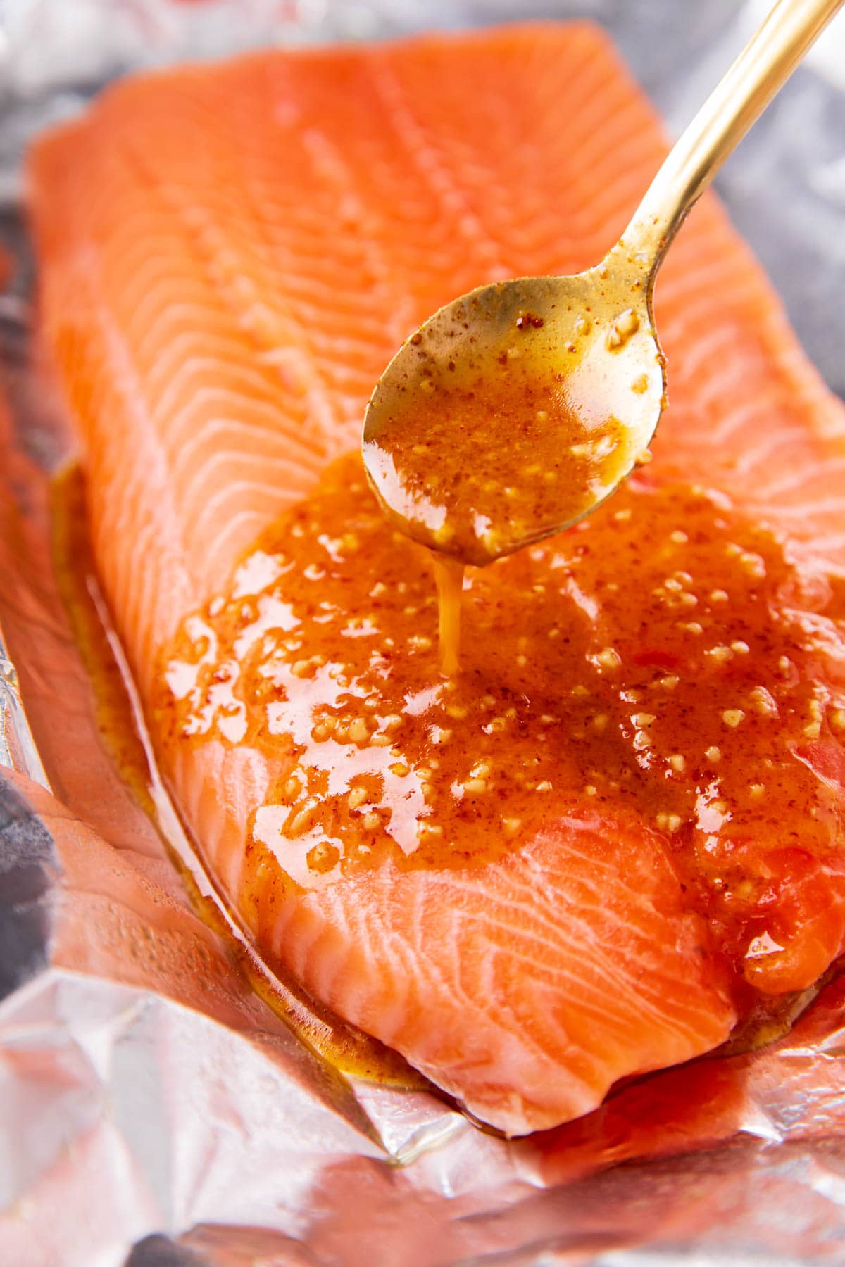 A photo showing How to Make Honey Mustard Salmon - someone spooning sauce over salmon in a foil packet.