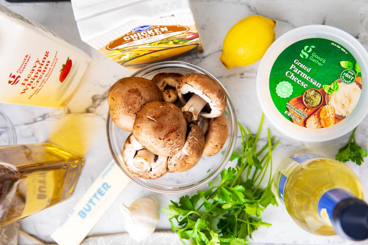 Mushroom Sauce ingredients including butter, mushrooms, garlic, dry white wine, chicken broth, heavy cream, lemon juice, Parmesan cheese and olive oil.