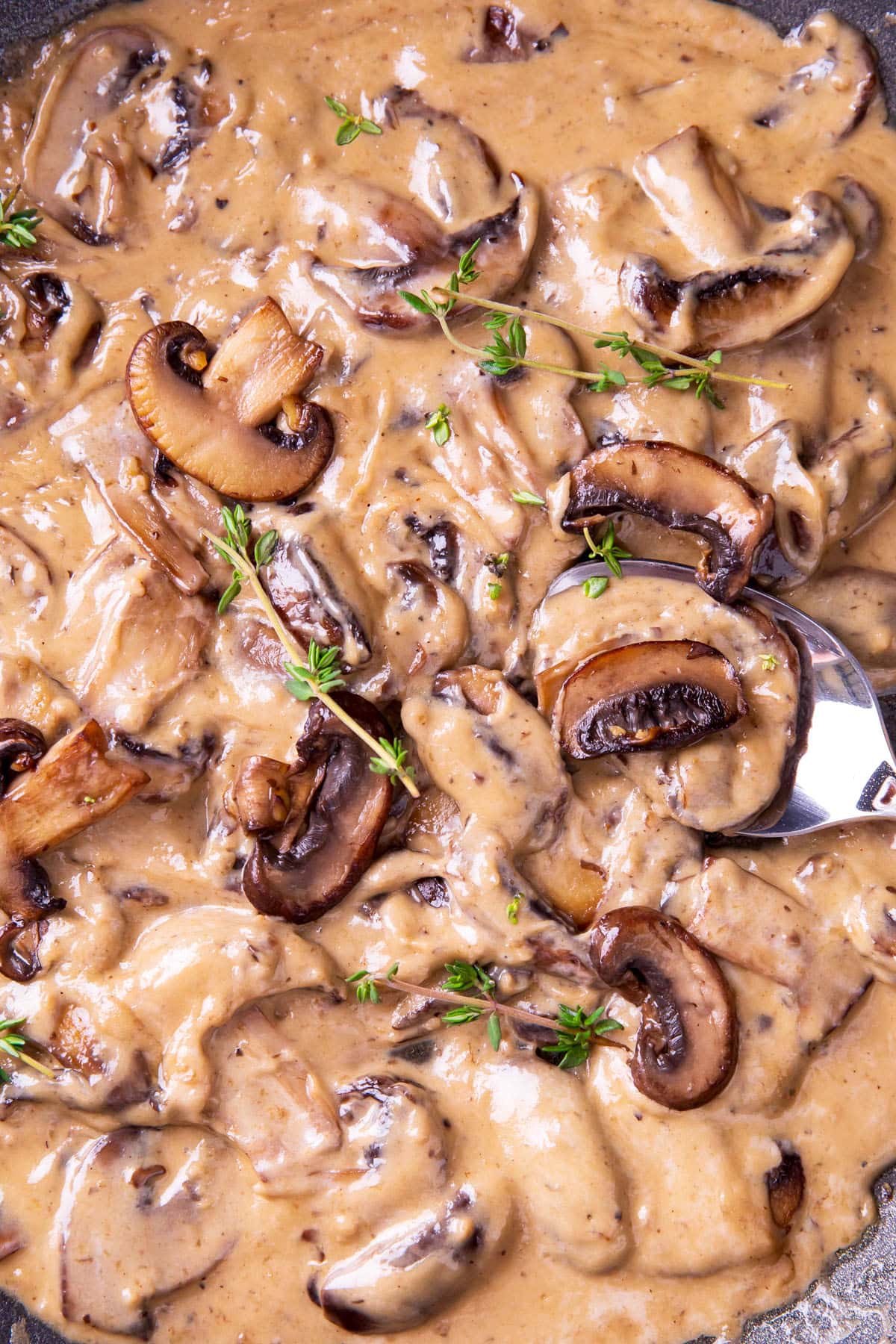Someone spooning this homemade sauce recipe for ravioli and chicken with rosemary garnish.