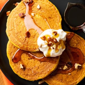 Overhead photo of fluffy Pumpkin Pancakes topped with maple syrup, whipped cream, and pecans