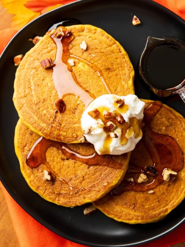 Overhead photo of fluffy Pumpkin Pancakes topped with maple syrup, whipped cream, and pecans