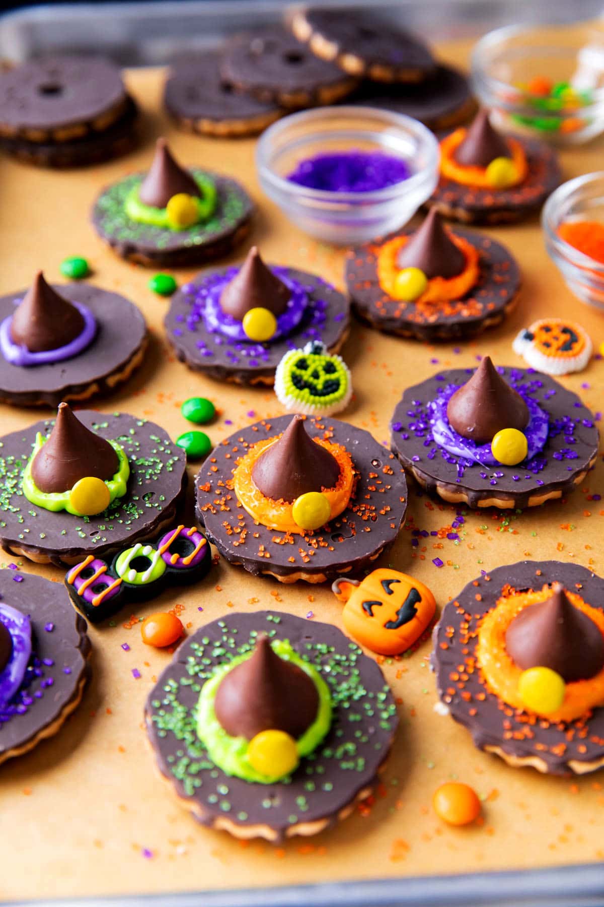 A lined cookie sheet topped with Witch Hat Cookies, Halloween toppers saying "Boo!" and Happy Halloween with bowls of candies and sanding sugar.