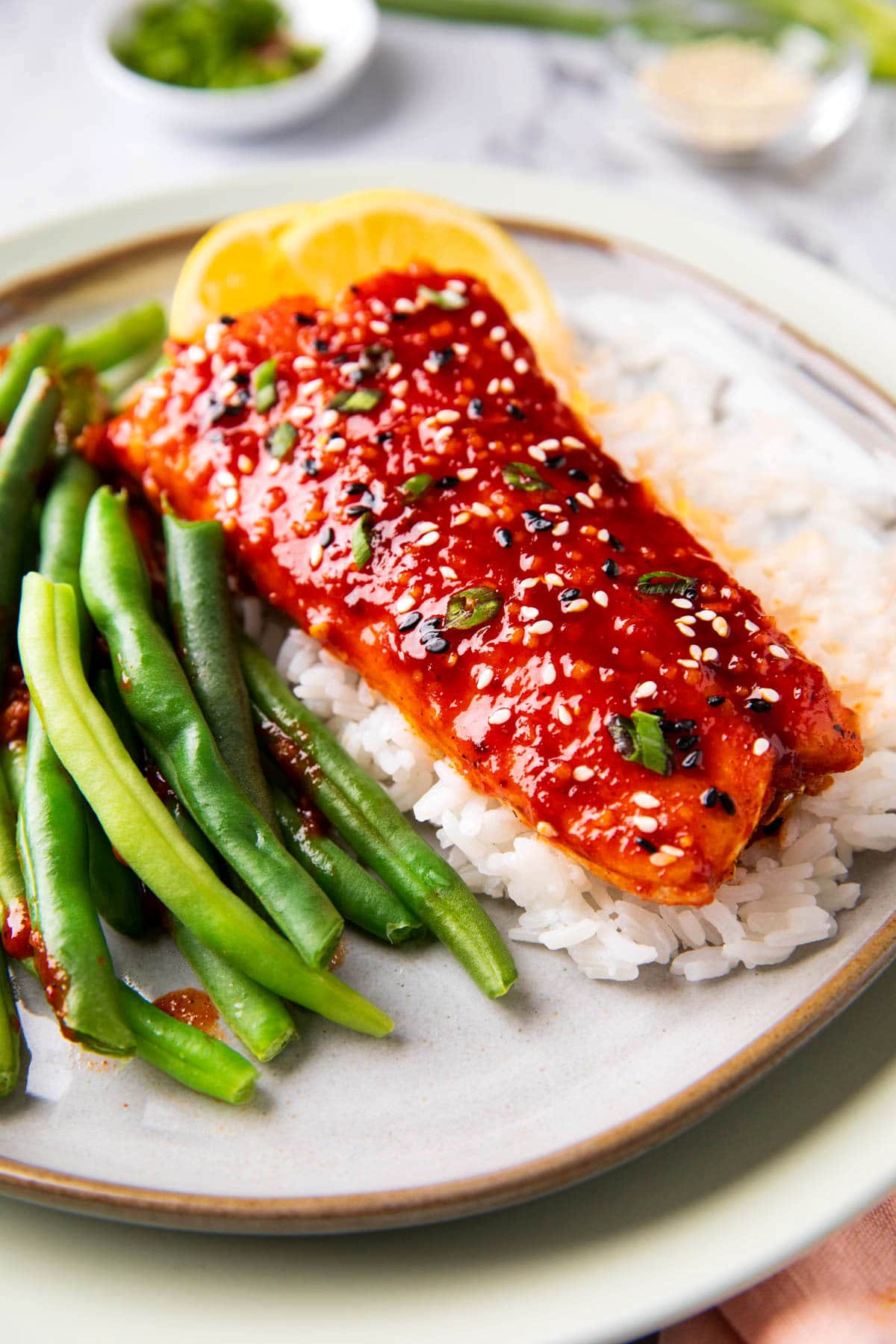 Gochujang salmon is swicy and served on a bed of white rice with black and white sesame seeds and sliced green onion.