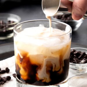 Close up of someone pouring milk from a jigger over coffee liqueur to make a White Russian