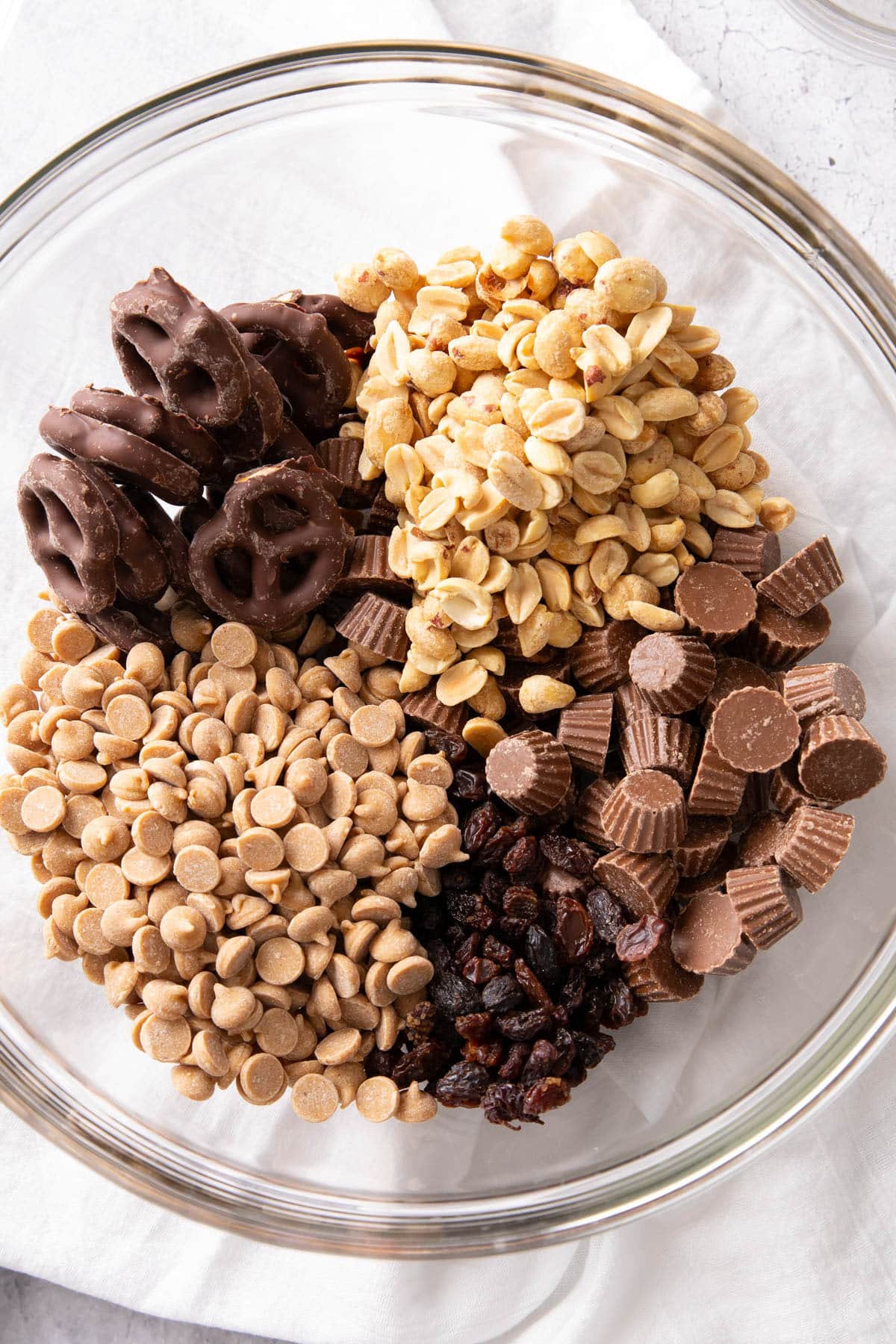 Peanut butter trail mix with peanut butter chips, peanuts, peanut butter cups, and raisins neatly divided in a mixing bowl.
